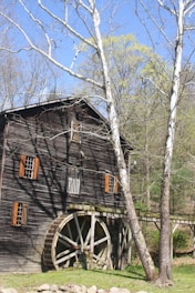 A rustic sawmill at Lingjerde Gard surrounded by lush green fields under a clear blue sky.