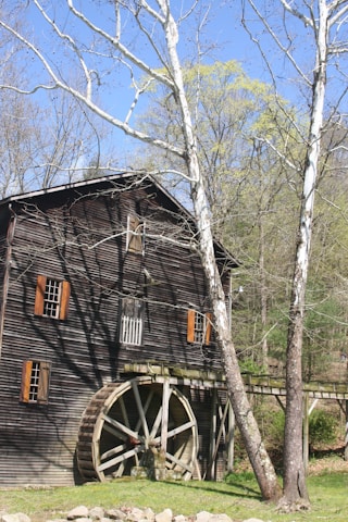 A rustic sawmill at Lingjerde Gard surrounded by lush green fields under a clear blue sky.