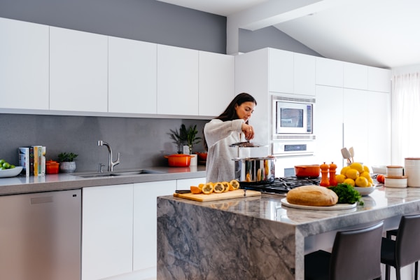 woman cooking in white and gray kitchen with dark marble island - Fall 2023 interior trends