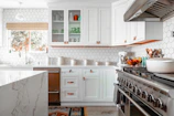 A bright kitchen with white cabinets, hexagonal wall tiles, and a marble island
