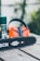 A chainsaw is resting on a wooden surface alongside an orange and black pair of safety earmuffs and a green spray can. The chainsaw bar features a 'Quick Stop' logo.