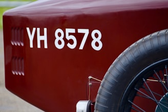 A close-up view of the rear section of a vintage vehicle, displaying a maroon color with a visible license number 'YH 8578'. The image focuses on the spare tire attached to the side and part of the vehicle body.