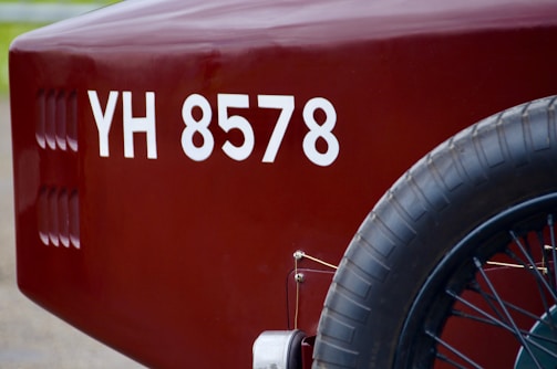 A close-up view of the rear section of a vintage vehicle, displaying a maroon color with a visible license number 'YH 8578'. The image focuses on the spare tire attached to the side and part of the vehicle body.