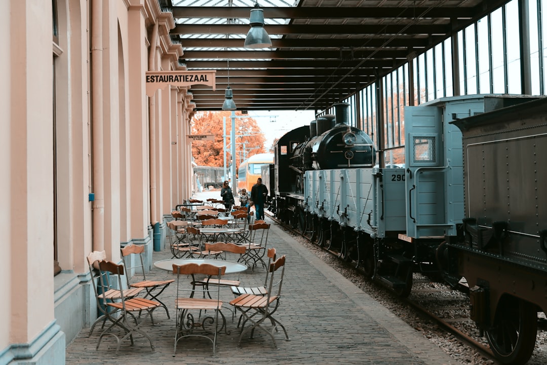 three people walking in alley with cafes and parked train,