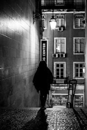 A shadowed figure in a dimly lit urban alleyway at night.