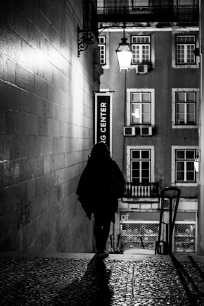 A shadowy figure walking through narrow streets of a small Occitanie village at night.