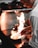 A chef is cooking in a professional kitchen, holding tongs and working over a stovetop with a bright flame. The chef wears a white coat and appears focused on the cooking task.