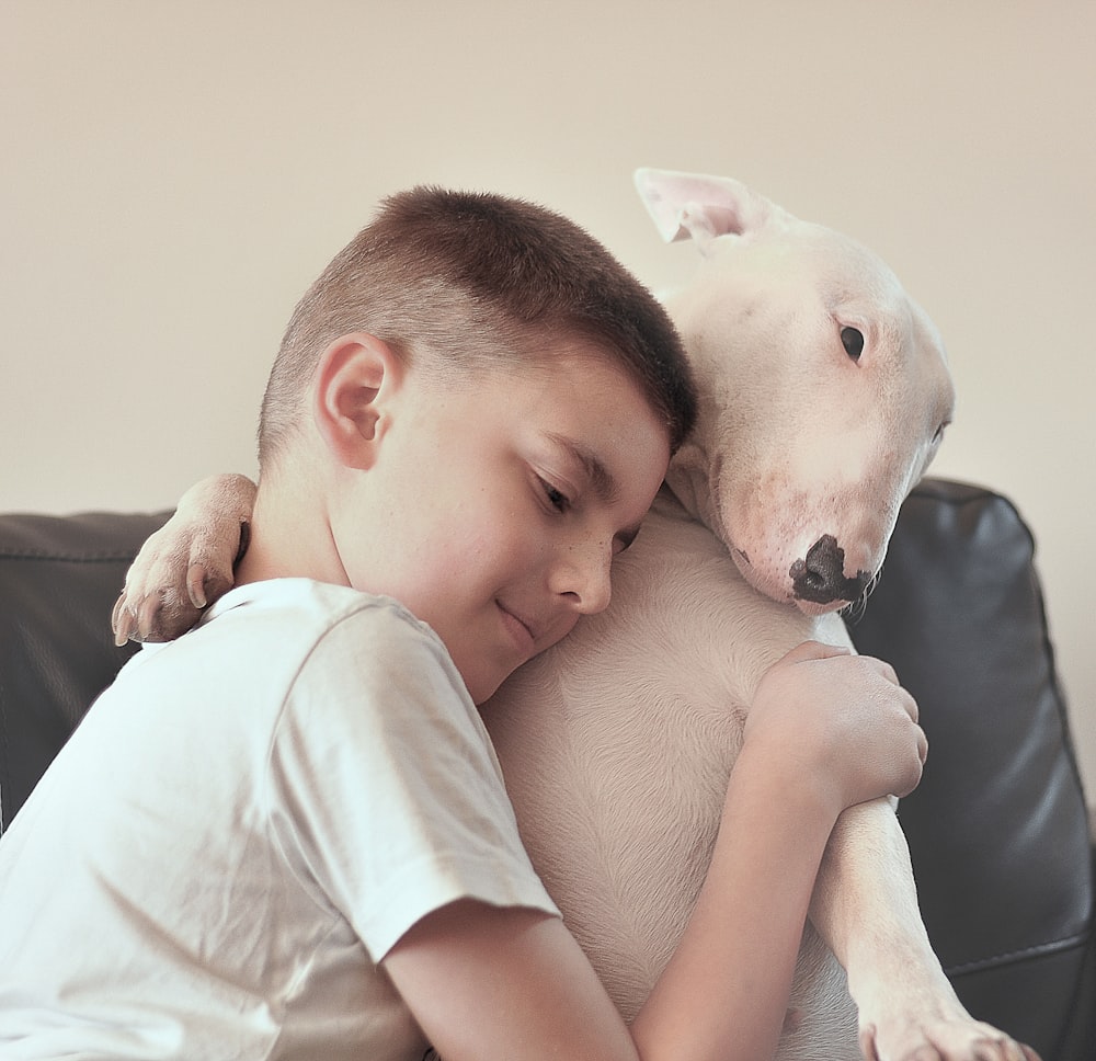 kid hugging a white dog in a room