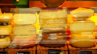 Various types of cheeses are stacked and arranged on wicker baskets, with labels indicating their names. The cheeses have different shapes and textures, and a warm, yellow and orange lighting enhances the presentation.