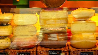 Various types of cheeses are stacked and arranged on wicker baskets, with labels indicating their names. The cheeses have different shapes and textures, and a warm, yellow and orange lighting enhances the presentation.