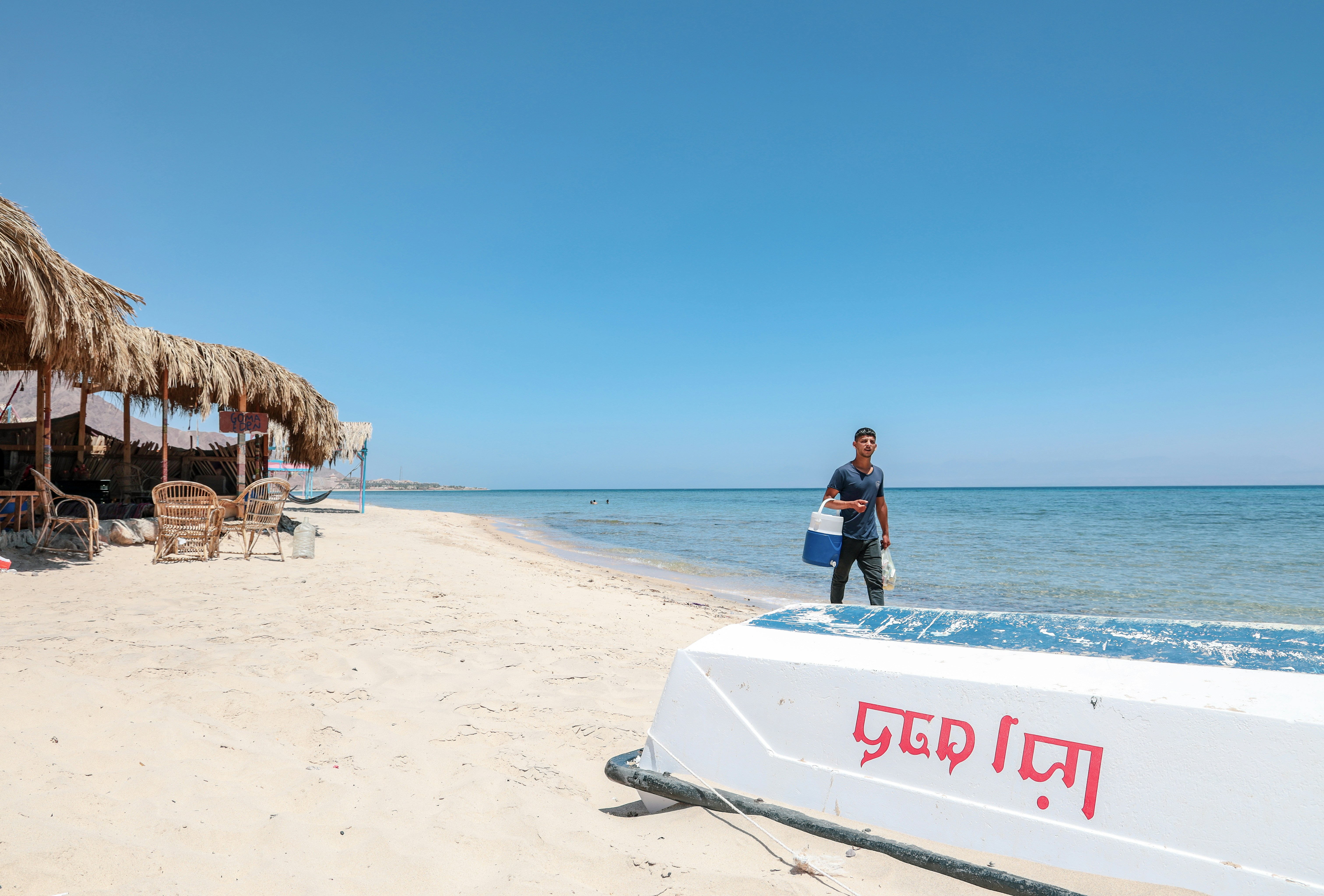 man carrying white and blue insulated beverage cooler in seashore