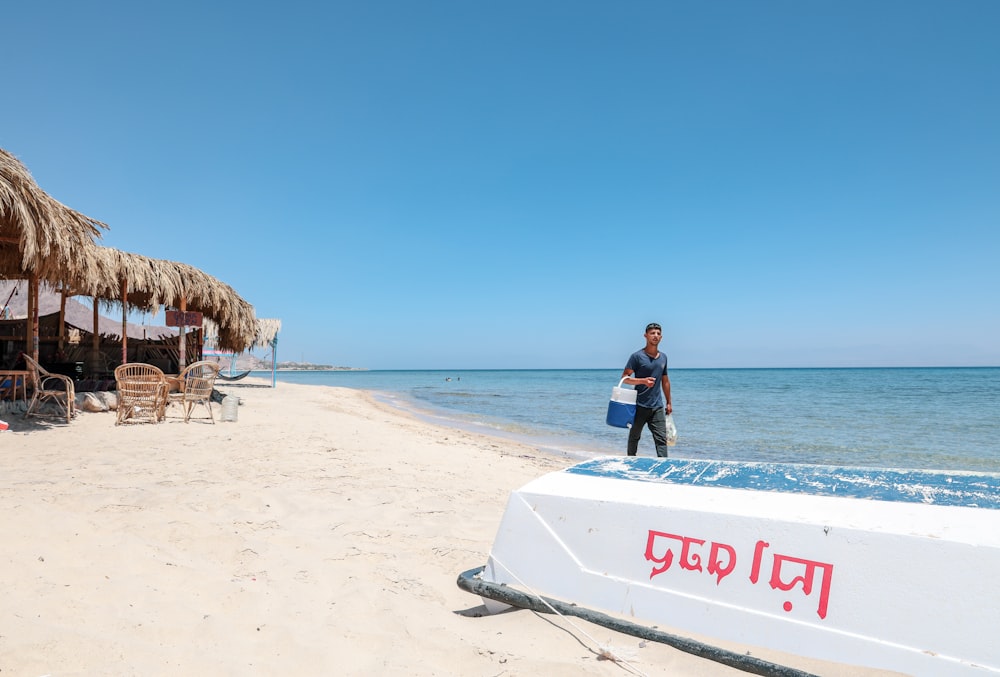 Hombre que lleva un enfriador de bebidas aislado blanco y azul en la orilla del mar