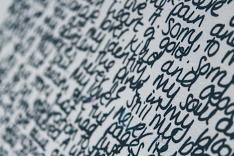Close-up view of handwritten text on a white surface. The words are written in a dense and flowing script, with limited spacing between each line and word. The ink appears to be a dark blue or black color, creating a stark contrast against the light background.