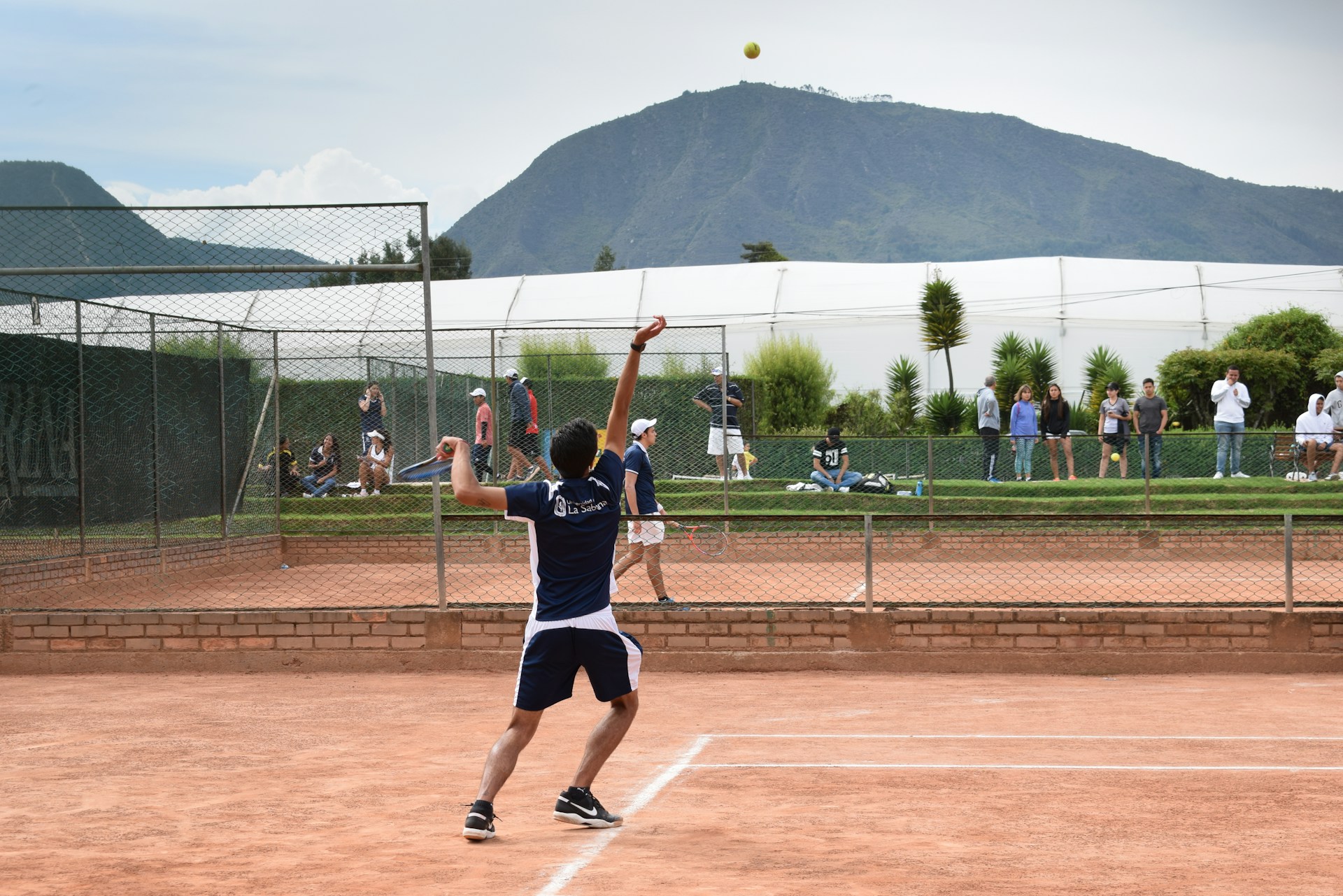 A dynamic tennis match moment capturing a player mid-serve with a packed stadium in the background.
