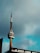 A tall communication tower with a distinctive circular structure near the top stands against a cloudy sky. The lower part of the tower is connected to a building with large windows.