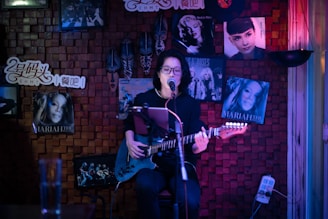 A young person happily playing an acoustic guitar in a cozy room filled with music posters.