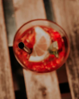Close-up of a vibrant cocktail with a slice of lime and a tiny umbrella on a wooden table.