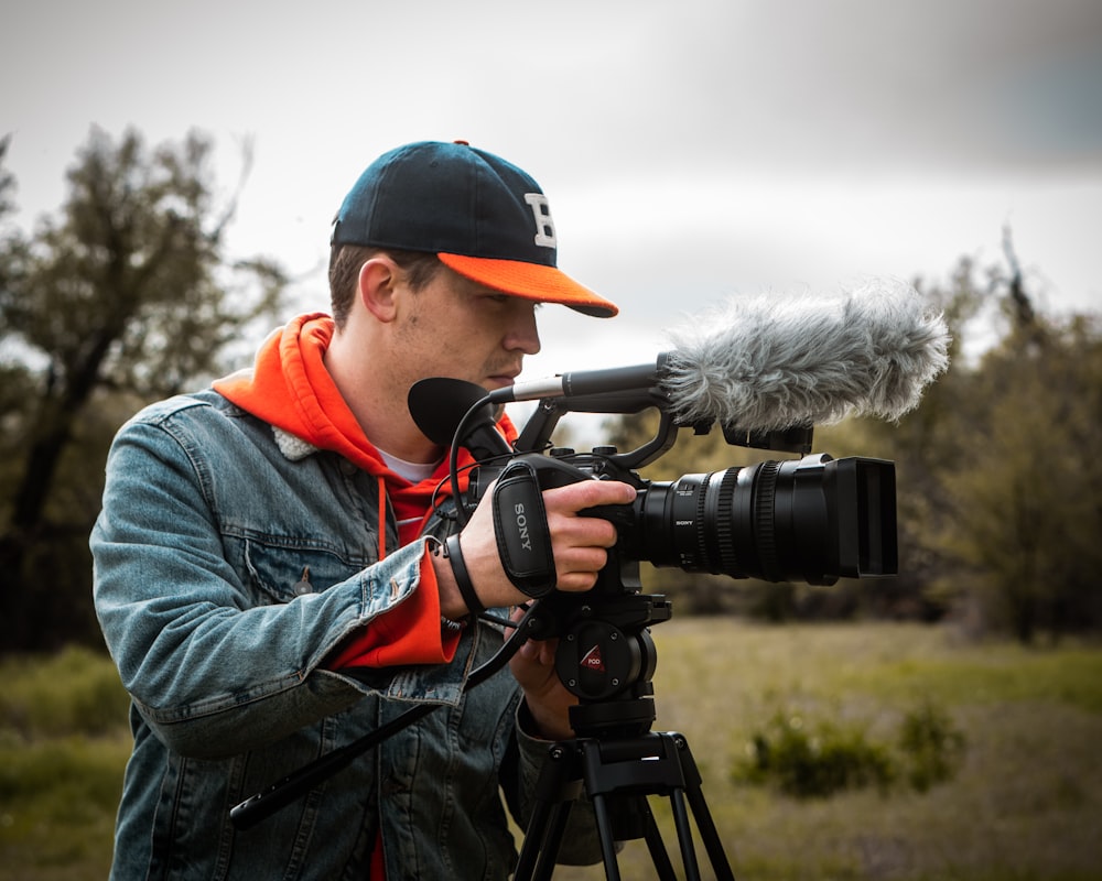 man standing and holding video camera on tripod stand near trees