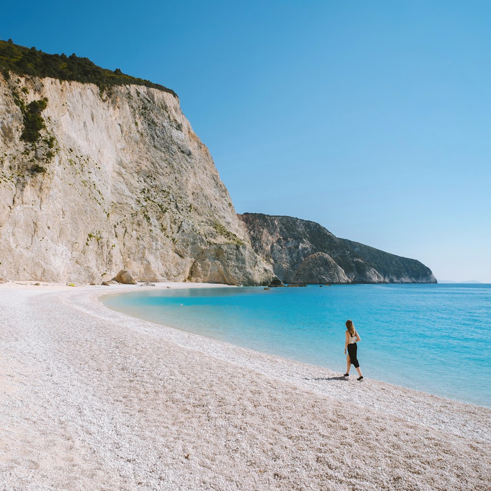 uma pessoa em pé em uma praia ao lado de um penhasco