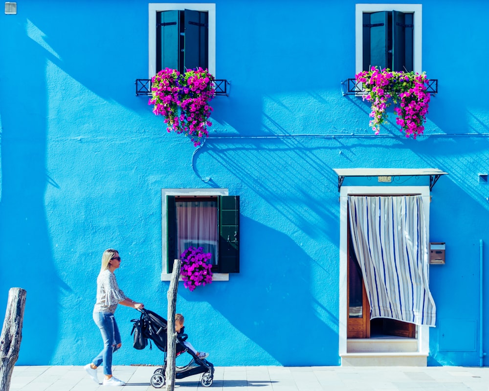 a woman pushing a stroller past a blue building