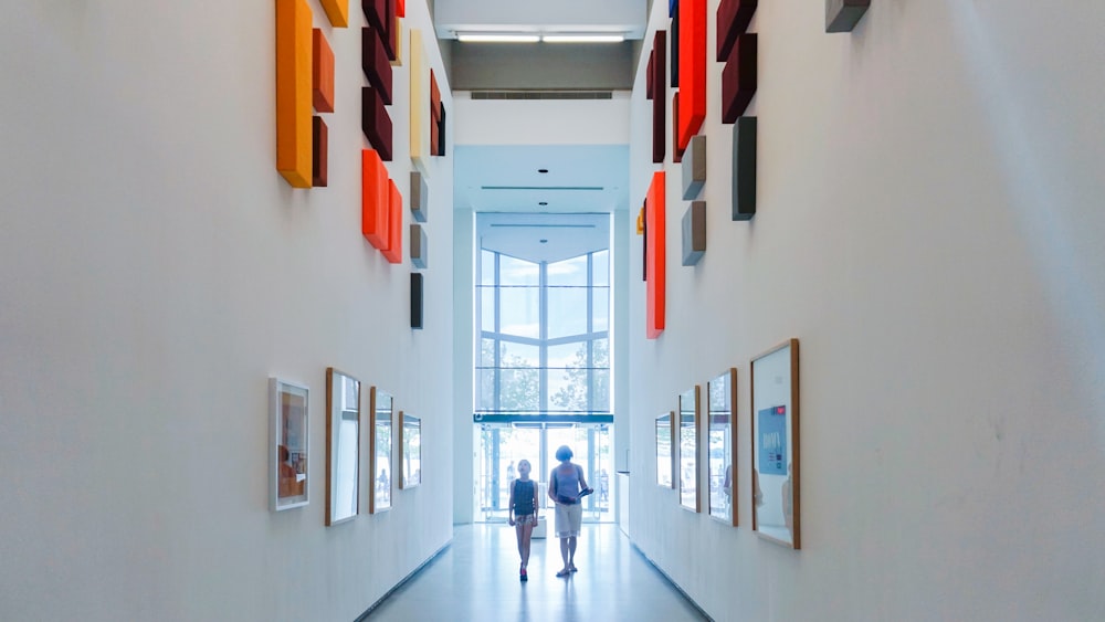 two person walking between white walls