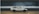 A white and black toy car with Japanese characters on the side is placed on a wooden surface. The background is blurred, focusing attention on the car model, which resembles a classic sports car design with compact dimensions.