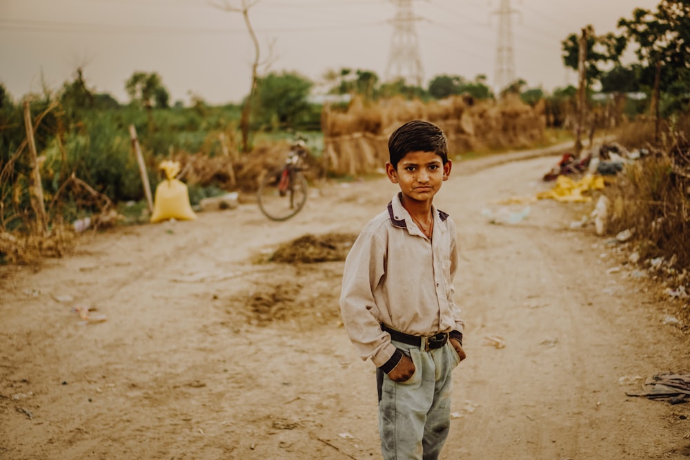 boy in grey dress shirt standing in the middle of dirt road