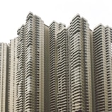 A cluster of modern high-rise apartment buildings with numerous balconies and uniform architectural design. The buildings feature a neutral color scheme and numerous windows, creating a repetitive and geometric pattern.