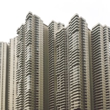 A cluster of modern high-rise apartment buildings with numerous balconies and uniform architectural design. The buildings feature a neutral color scheme and numerous windows, creating a repetitive and geometric pattern.