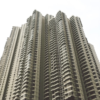 A cluster of high-rise residential buildings with numerous balconies and windows. The architecture is modern with a repetitive pattern of protruding balconies, creating a sense of uniformity. The sky is overcast, contributing to a neutral or muted appearance.