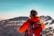 Close-up of a hiker adjusting a bright orange tov outdoor backpack strap against mountain scenery.