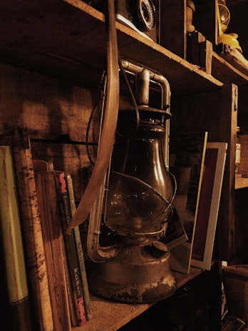 Close-up of a beautifully aged brass lamp and a stack of well-loved vintage books on a wooden shelf.