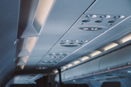 Airplane cabin ceiling with passenger service units, air vents, and illuminated no-smoking and seatbelt signs