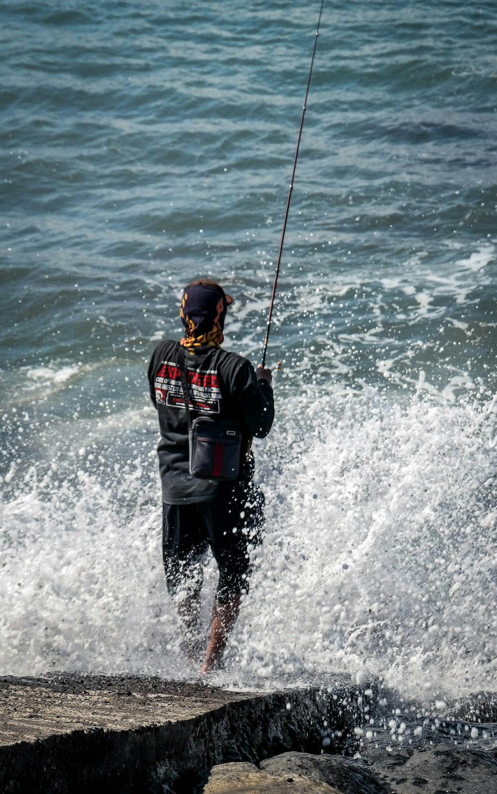 homme portant une chemise noire pêchant sur l’océan