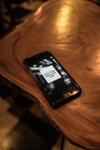 A smartphone is placed on a wooden surface with a screen displaying a message. The lighting is dim, casting a warm glow over the wood, creating a cozy and relaxed atmosphere.
