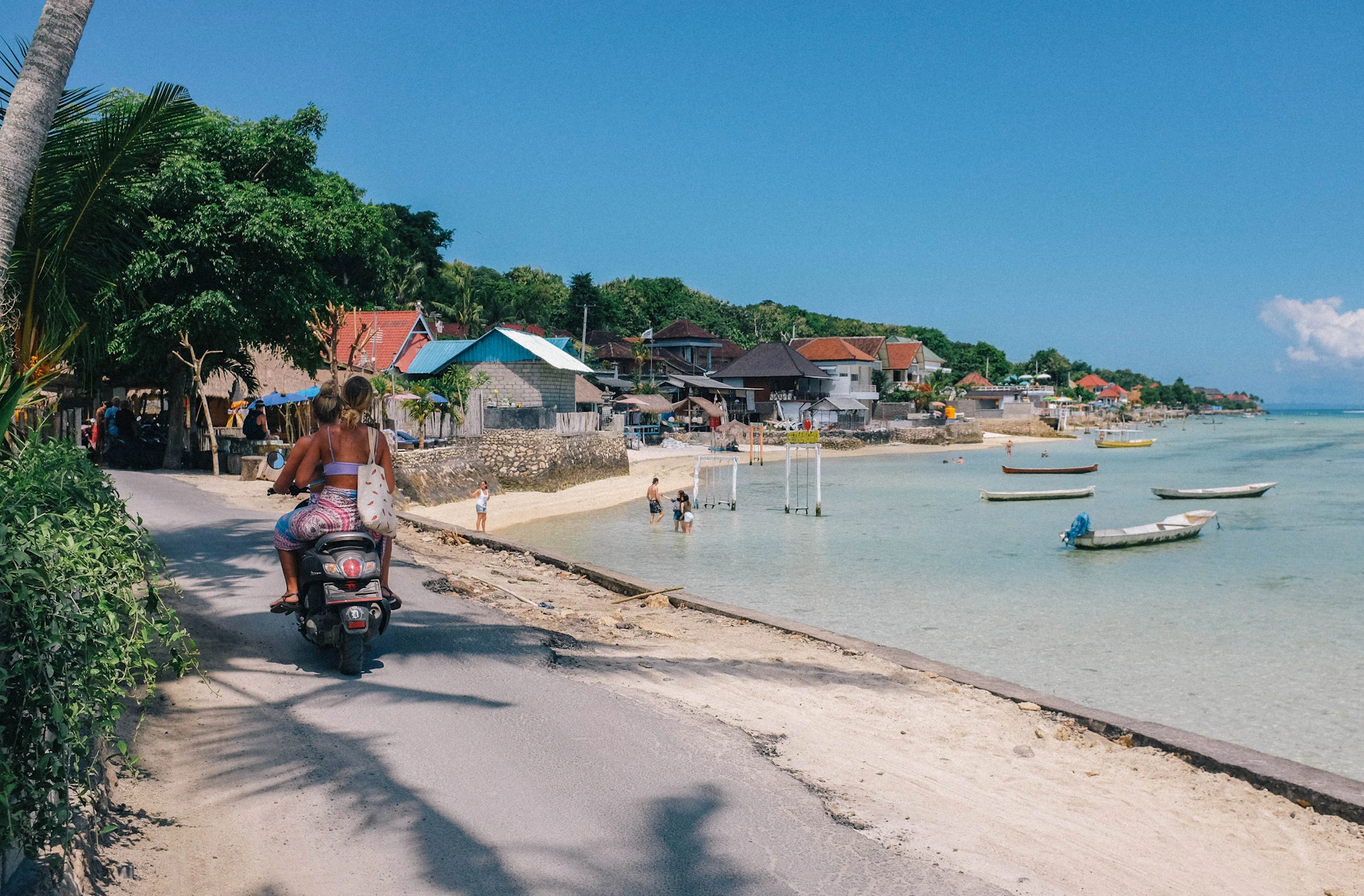 A happy traveler riding a sleek scooter along a scenic coastal road in Bali, with the ocean sparkling beside them.
