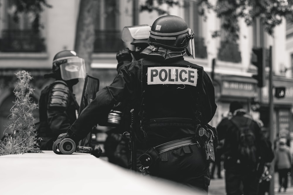 Foto en escala de grises de la policía de pie y apoyada en la pared