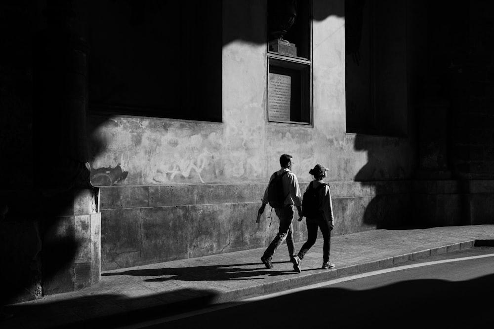 Foto em escala de cinza do homem e caminhando perto do edifício de concreto