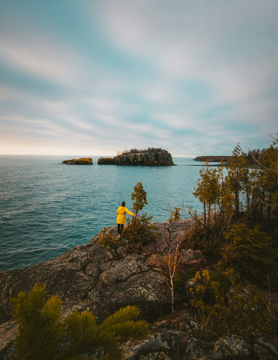 person in yellow top standing on rock cliff beside sea