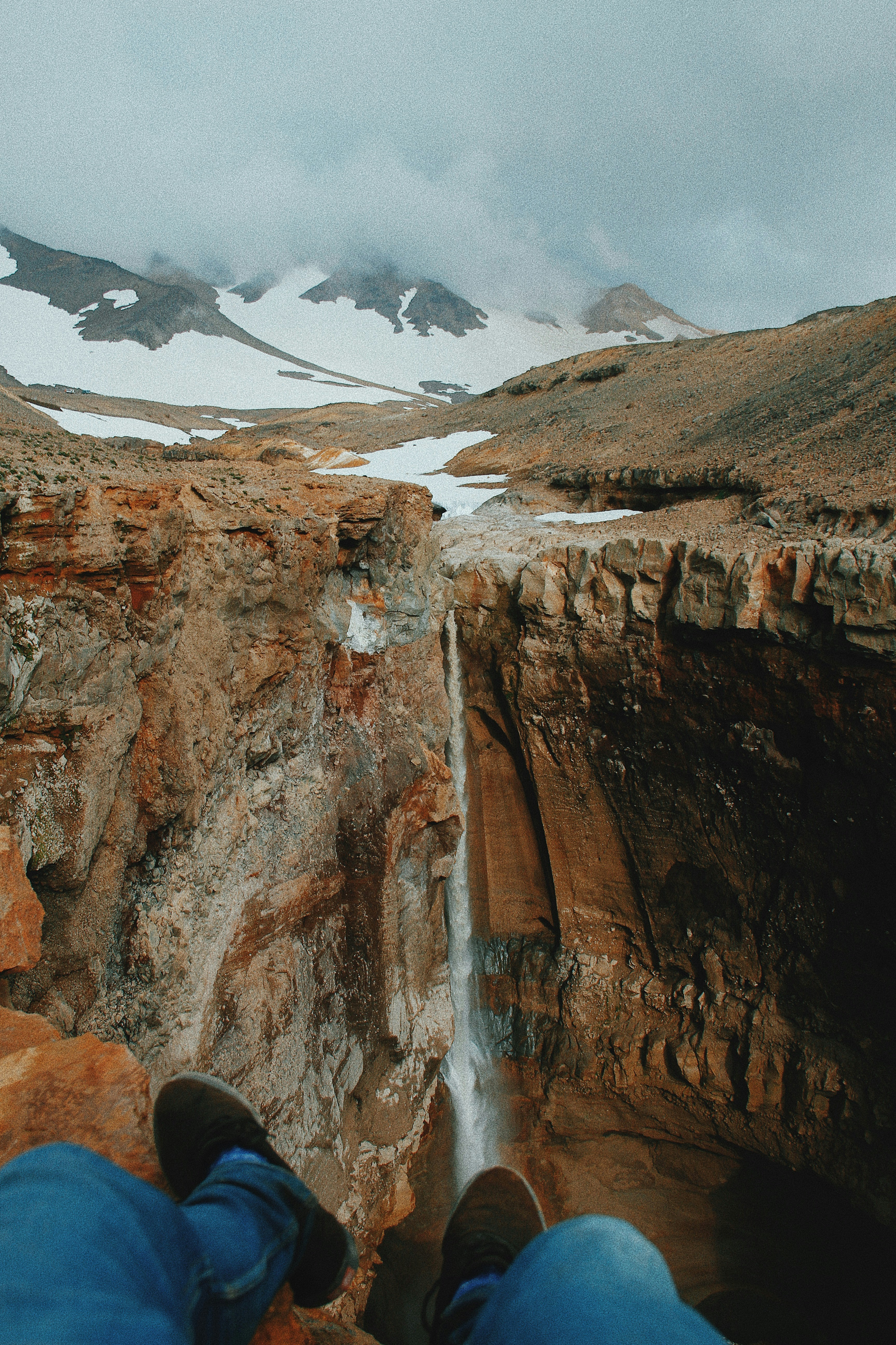 man sitting on rock formation near waterfall during daytime