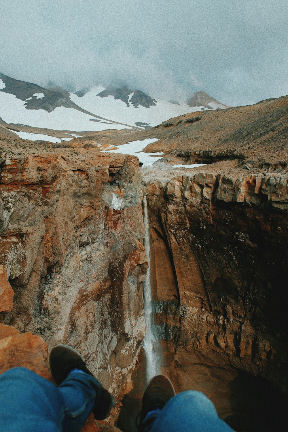 man sitting on rock formation near waterfall during daytime