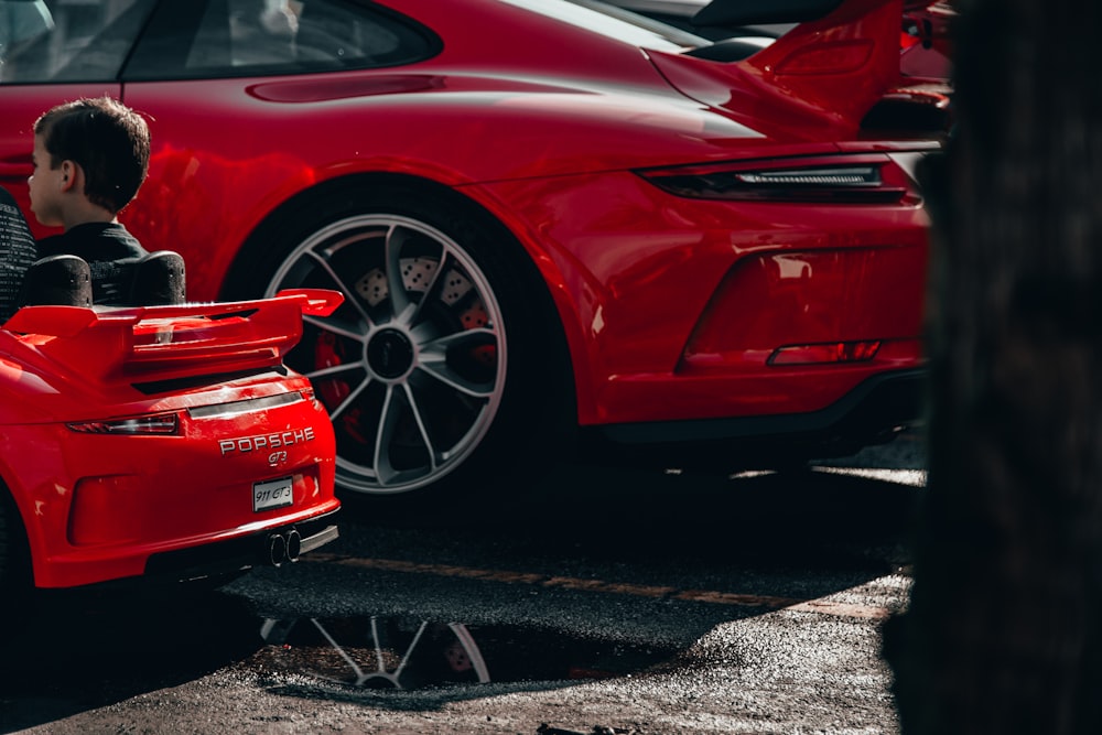 boy sitting on red ride-on car beside red car