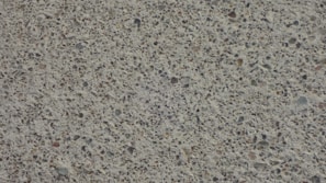 A close-up view of a textured concrete surface with small stones embedded, creating a speckled appearance.