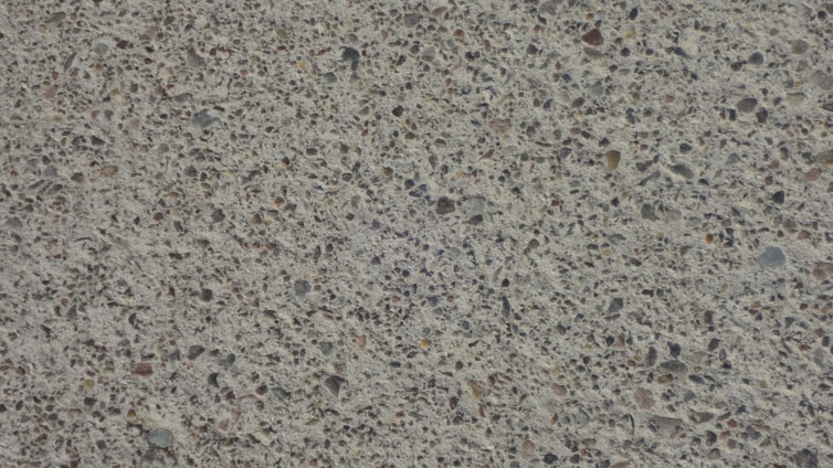 A close-up view of a textured concrete surface with small stones embedded, creating a speckled appearance.