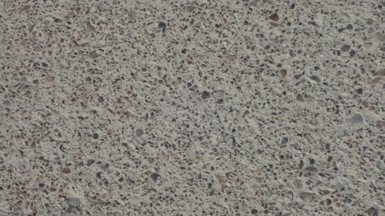 A close-up view of a textured concrete surface with small stones embedded, creating a speckled appearance.