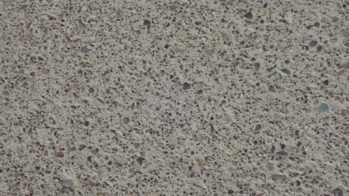 A close-up view of a textured concrete surface with small stones embedded, creating a speckled appearance.