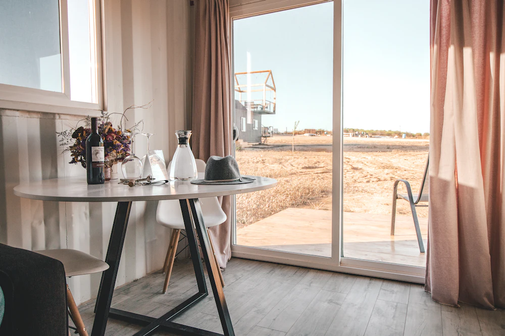 Wine bottle and glass on a side table beside a shuttered window