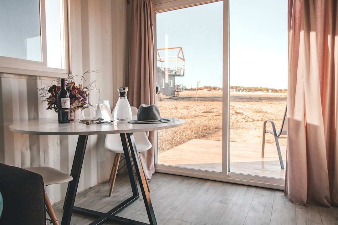 wine bottle near glass on end table beside closed window,