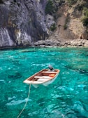 A small boat anchored near a hidden cove with crystal-clear turquoise water and rocky cliffs.