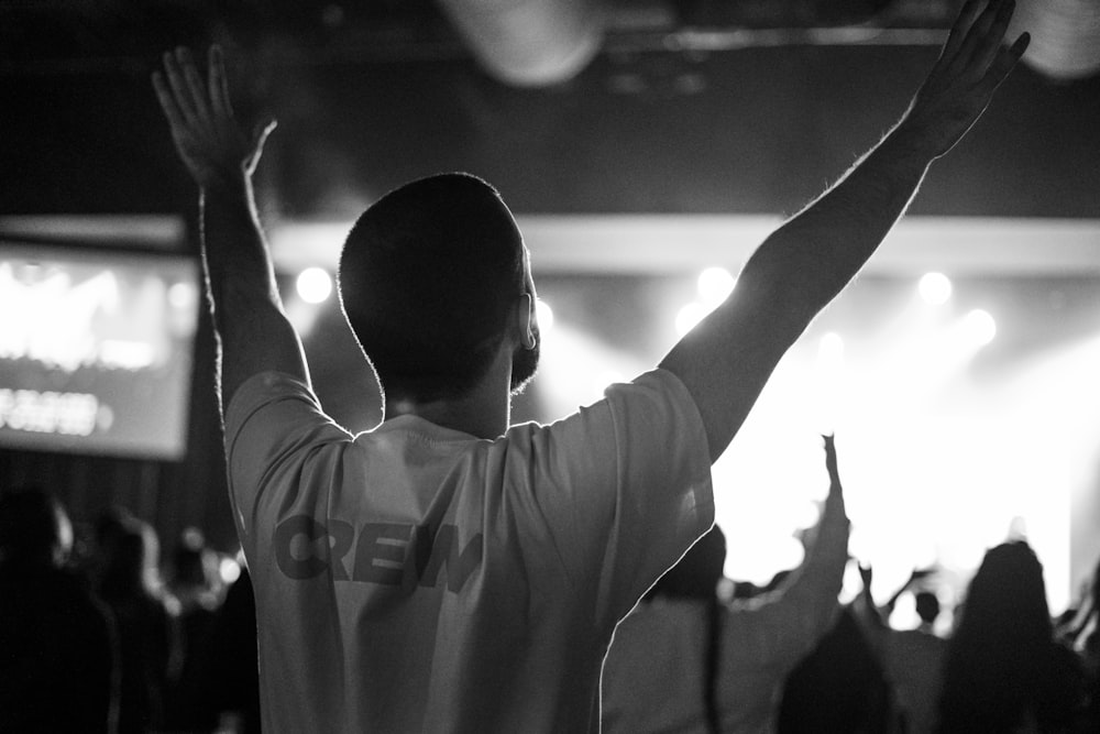 grayscale photo of man in crew-neck shirt raising both hands